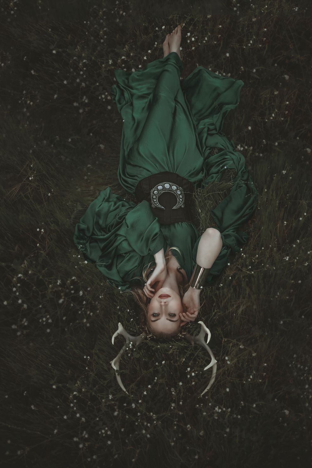 Woman in green Victorian dress lying in dark grass field, aerial view, artistic fantasy photography.