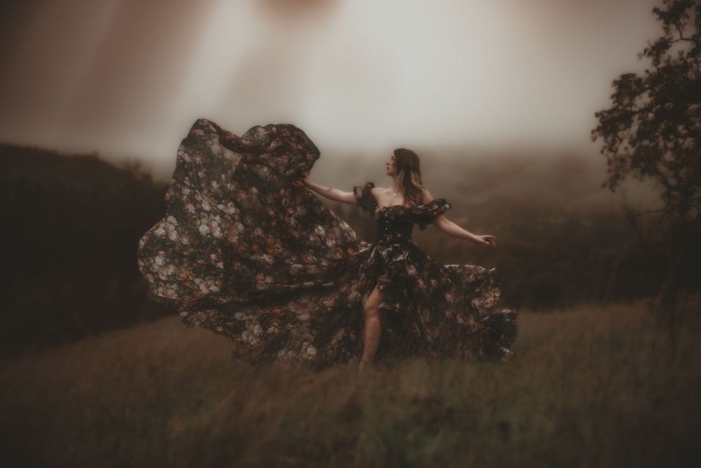 A person in a flowy dress dances through a misty field at sunset creating a dreamy, ethereal scene.