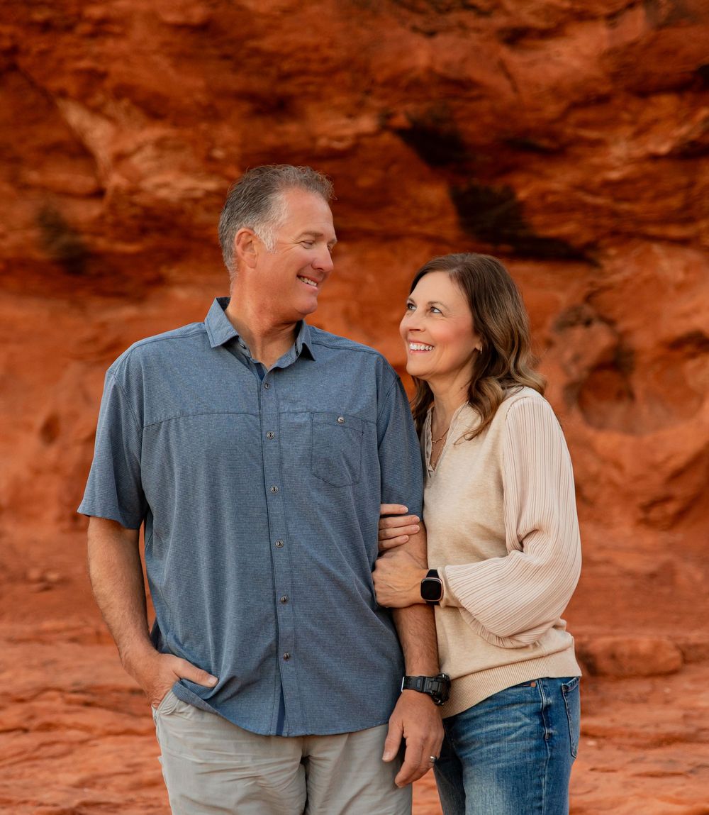 A couple shares a loving moment while standing against red rock formations in a desert landscape.