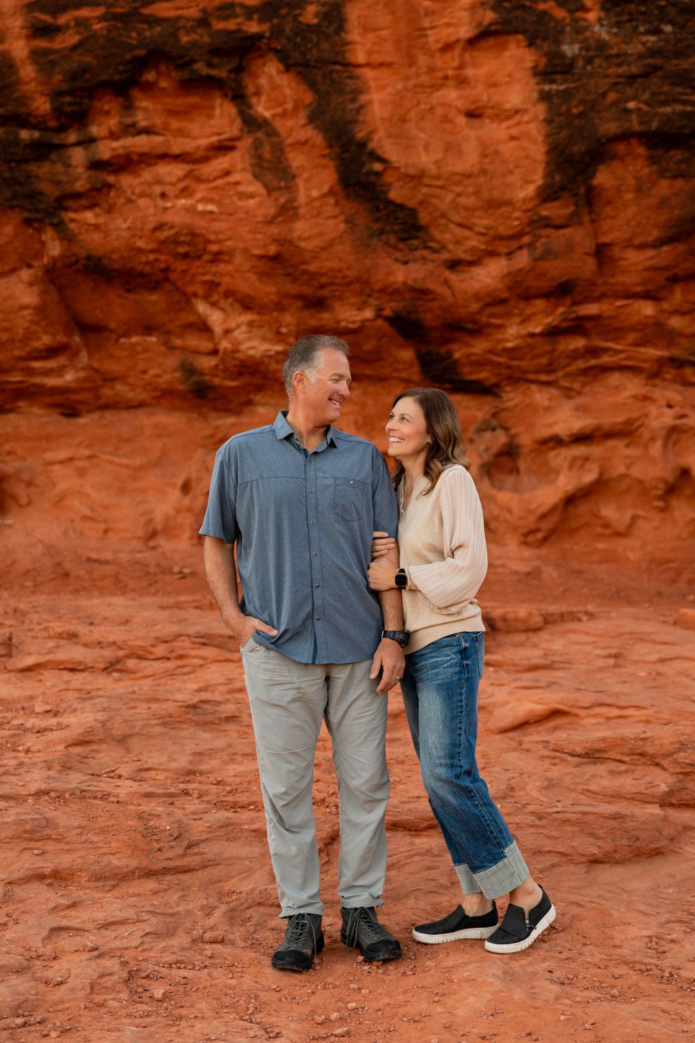 A couple stands together against vibrant red rock formations in a desert landscape. best photographer in southern utah