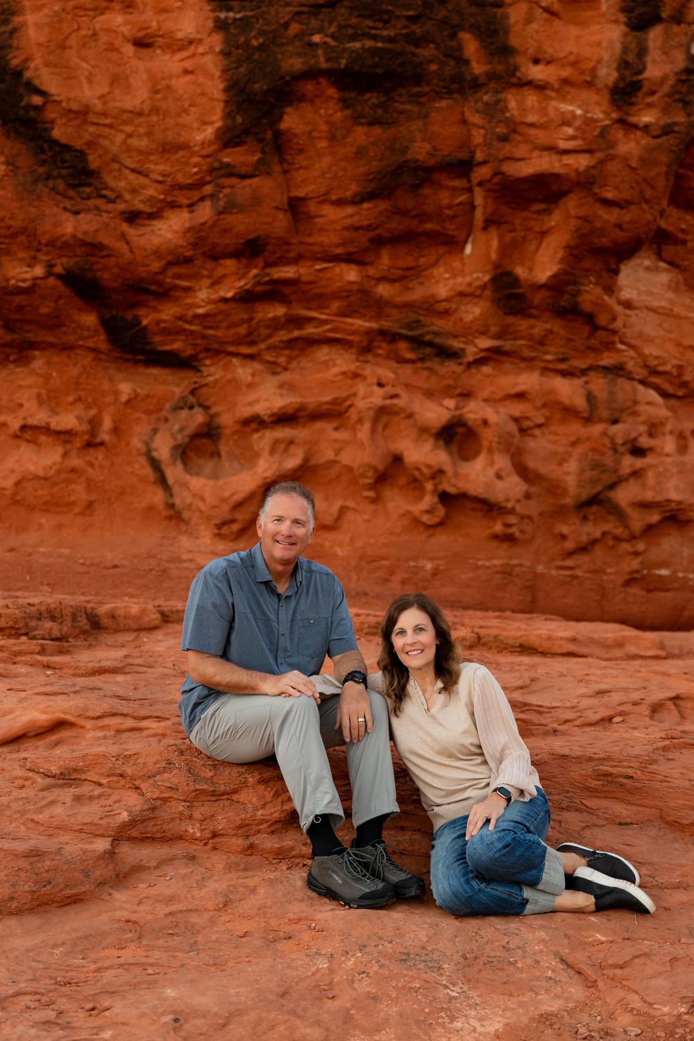 Two people sit together on vibrant red sandstone rocks in a scenic desert landscape. best photographer in southern utah