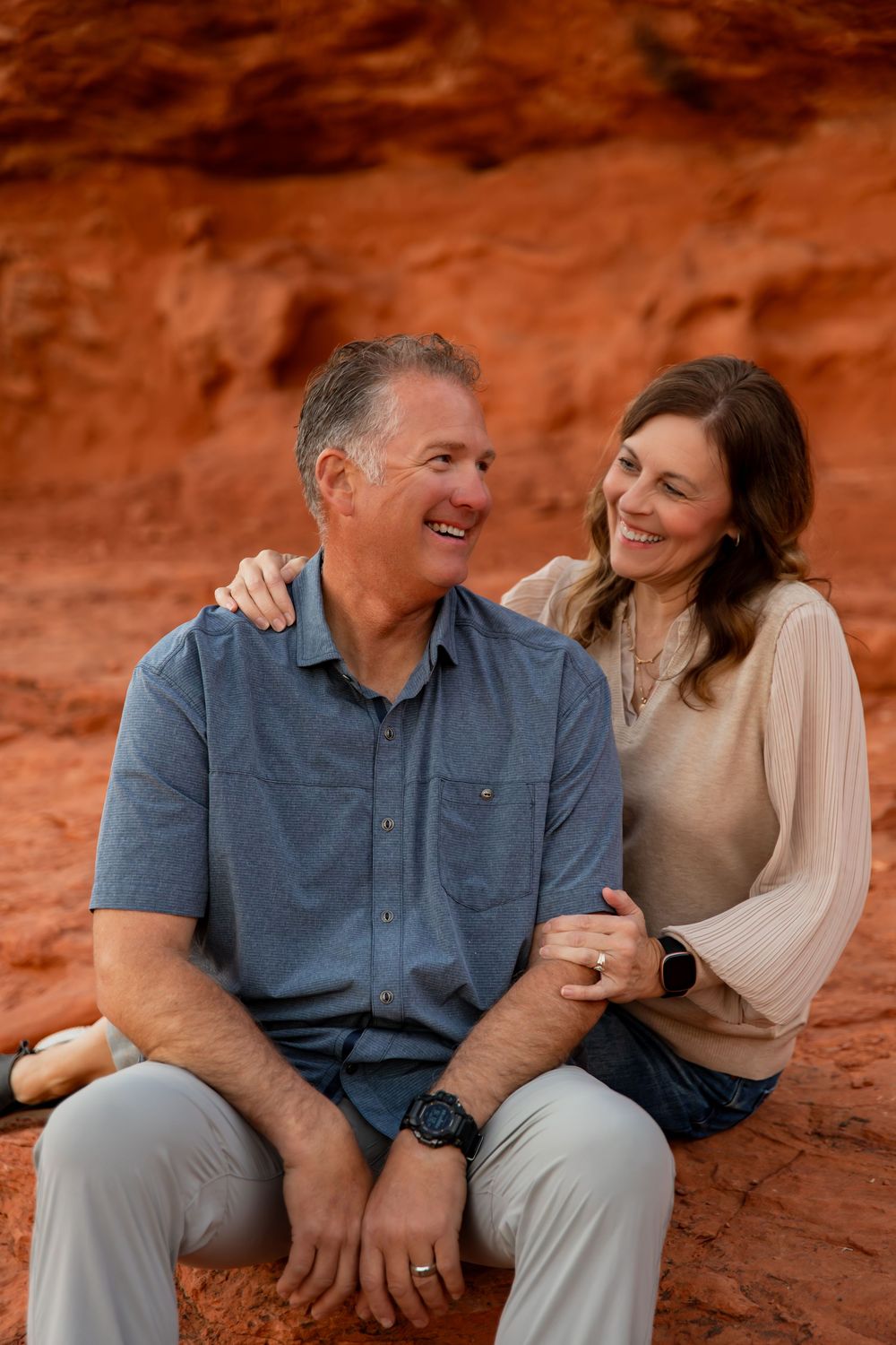Happy couple sitting together and laughing against red rock formations in a desert landscape. best photographer in southern utah