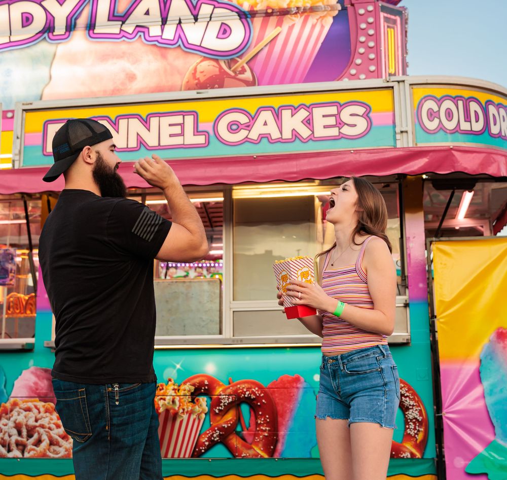 Couple enjoying funnel cakes and snacks at a colorful carnival food stand called Candy Land.