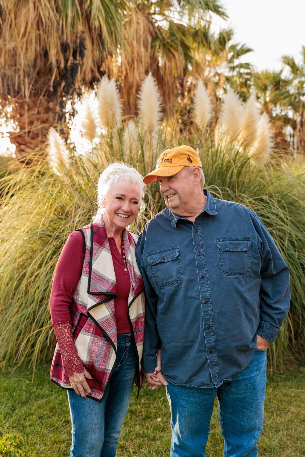 Senior couple holding hands and smiling while walking in a garden with ornamental pampas grass and palm trees. best photographer in southern