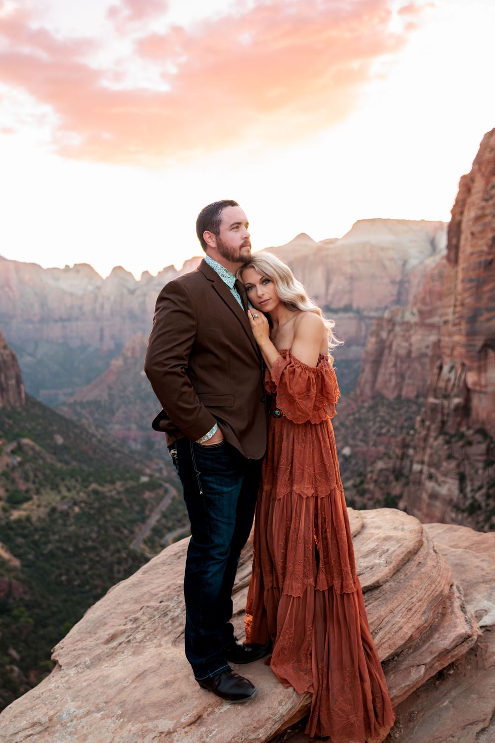 Couple embracing on a rocky overlook at Zion National Park during sunset, woman in rust boho dress.
