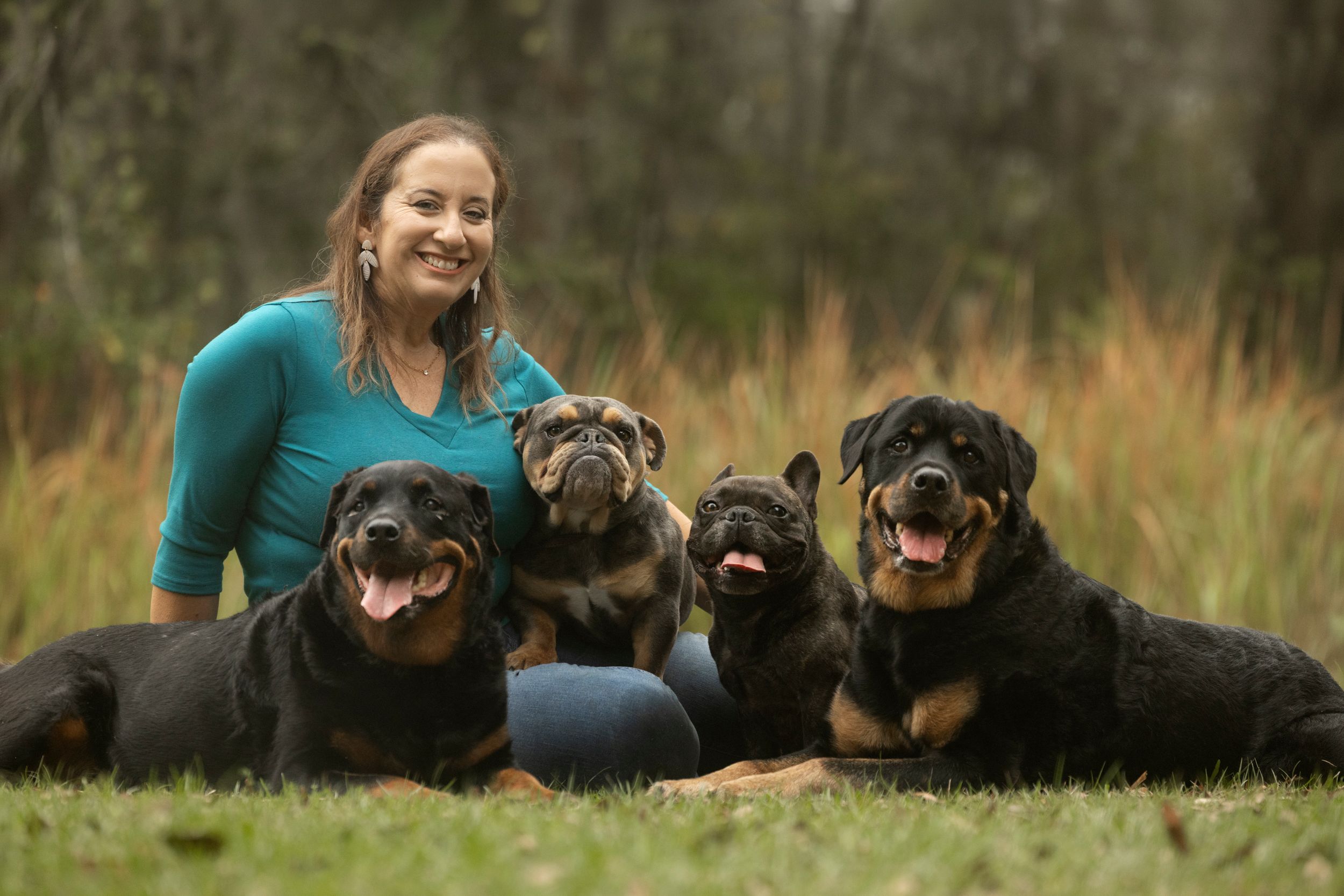 A woman sitting in a grassy park surrounded by her four rescue dogs of various breeds.