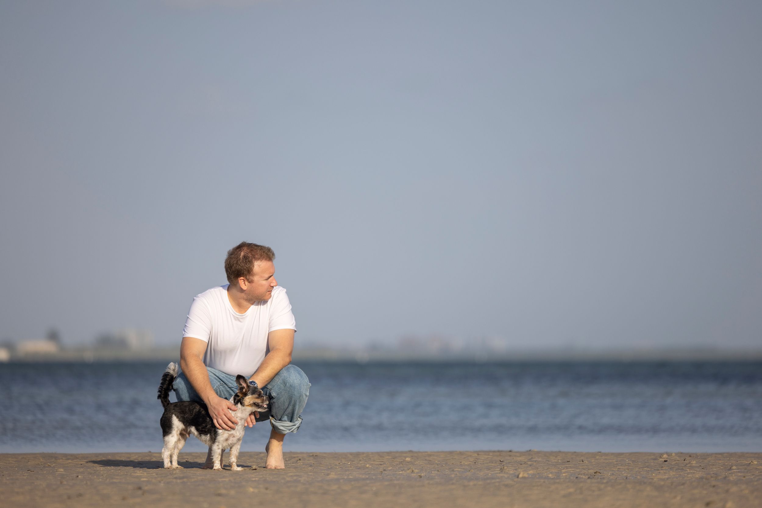 A dog dad and his pup sharing a quiet moment at the beach, looking in the same direction at the horizon.