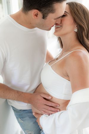 Intimate maternity photo of couple in white clothes sharing romantic moment.