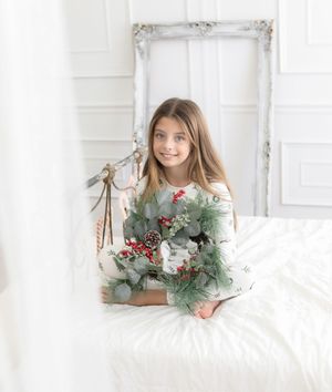 Young girl in white dress holding eucalyptus and berry branches in front of vintage frame.