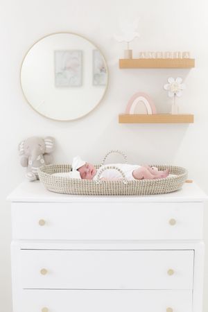 Minimalist nursery with round mirror, floating shelves and changing table holding sleeping baby.