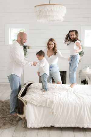 Family having fun jumping on white bed together in bright modern bedroom.