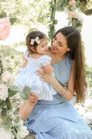 Sweet outdoor portrait of mother and child in blue and white dresses surrounded by delicate pink florals.