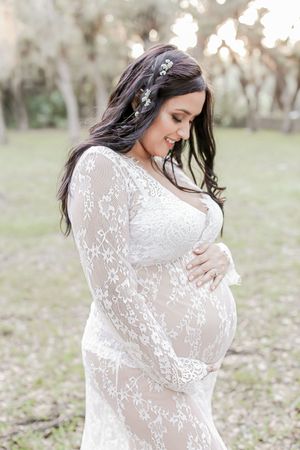Ethereal maternity portrait in a white lace dress with floral crown against a soft bokeh background.