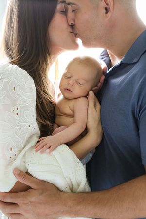 Intimate portrait of parents holding their sleeping newborn baby in soft natural light.