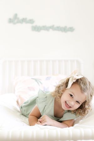 Candid portrait of smiling toddler in mint green outfit lying on striped bedding.