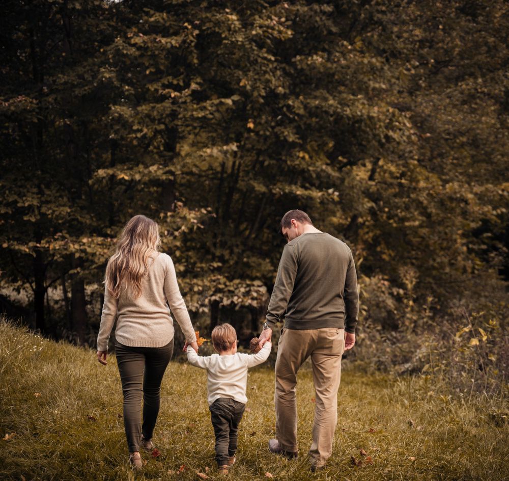 Family walking together holding hands on grassy hillside during autumn.