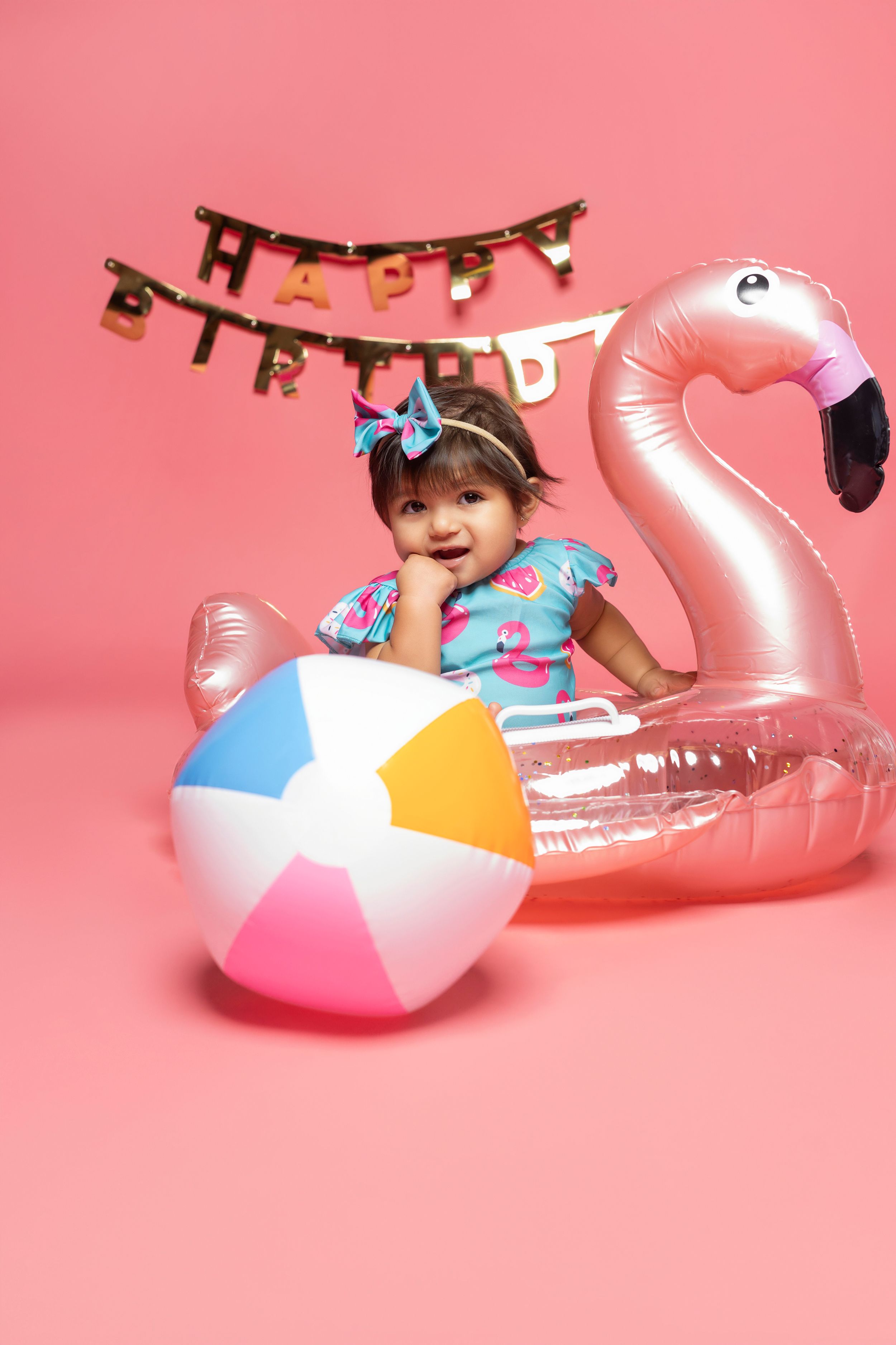 Colorful summer party scene with beach ball and pink flamingo float against coral background with Happy Birthday banner.