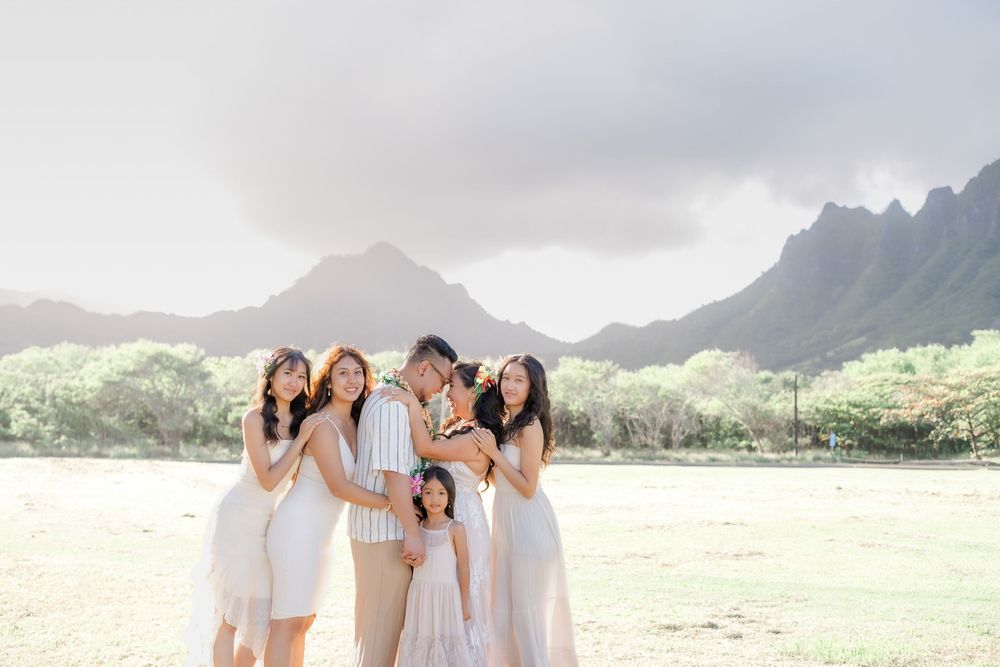 Group in white outfits posing together on a scenic beach with mountains in the background at sunset.
