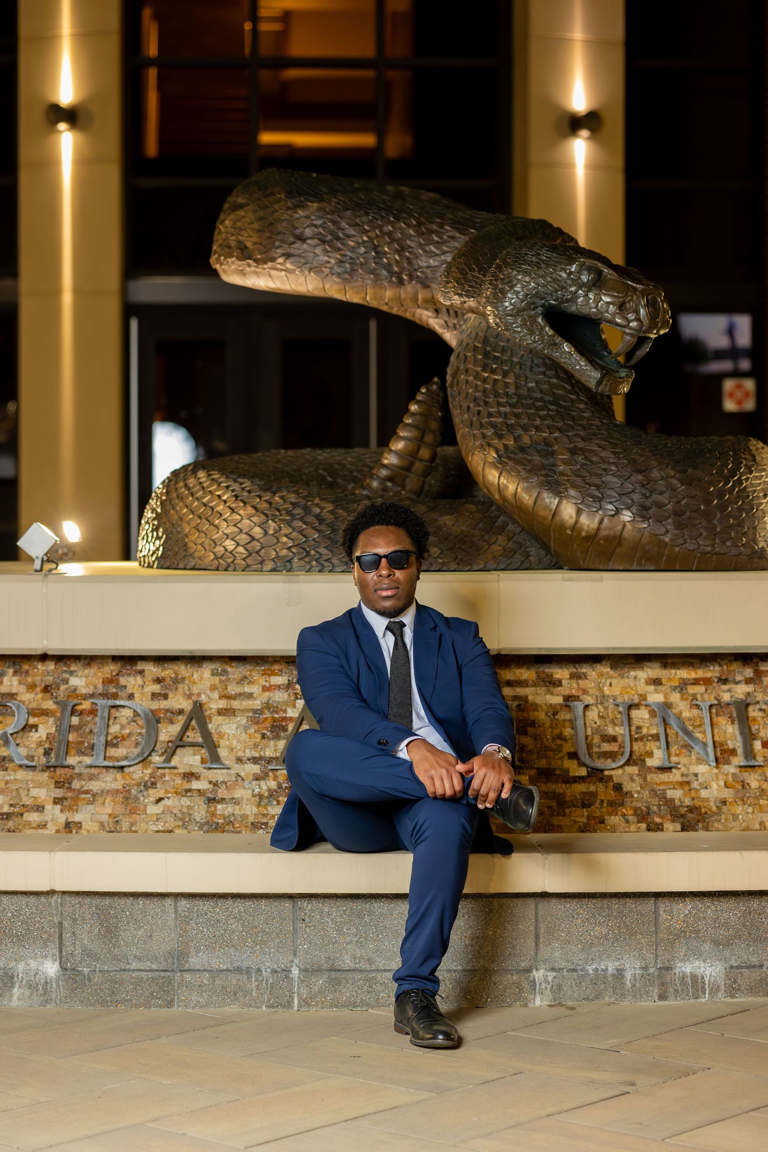 Professional portrait of businessman in blue suit seated beneath large snake sculpture.