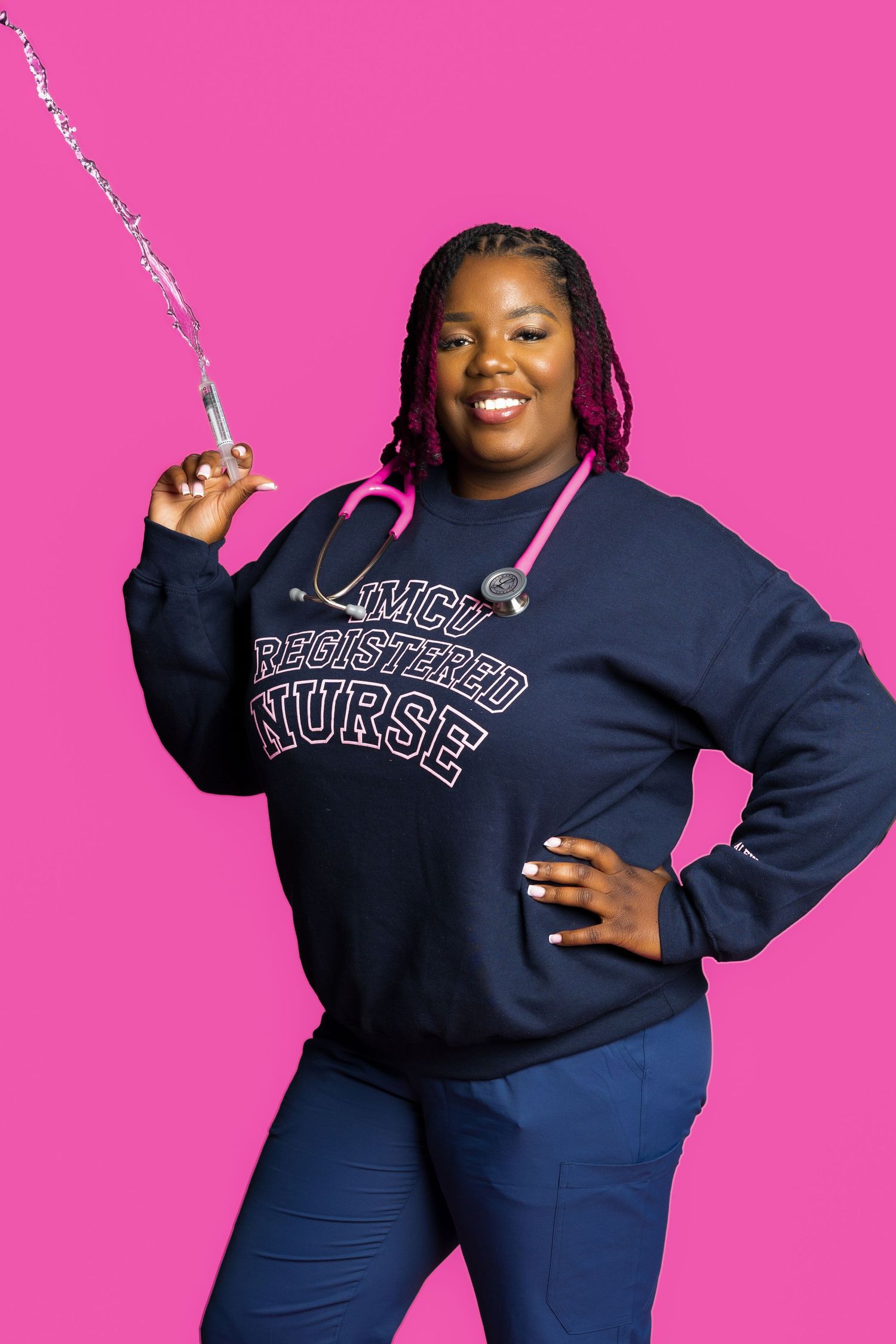 Nurse in navy sweatshirt poses with splashing water against pink backdrop.