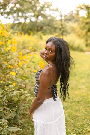 Birdy in a white dress poses joyfully in a garden setting with yellow flowers and greenery for her senior photos in Des Moines, Iowa.
