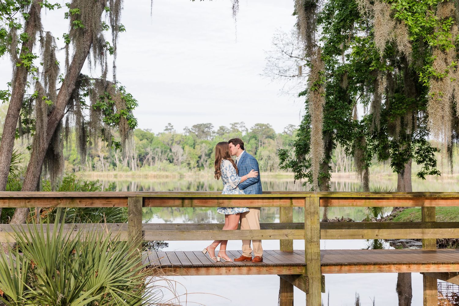 Wooden boardwalk stretching through lush coastal landscape with Spanish moss trees.