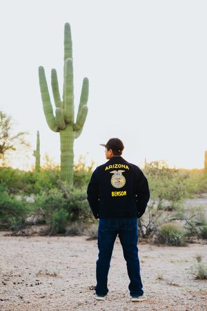 Person in FFA uniform stands against backdrop of saguaro cacti in Arizona desert.