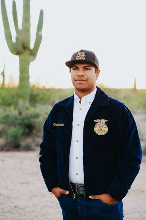 FFA member in official dress uniform poses in desert landscape with saguaro cacti.