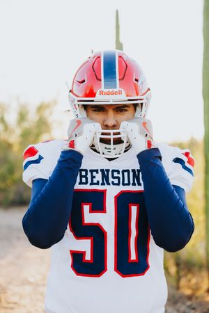 Football player wearing Benson jersey number 50 adjusts helmet in desert setting.