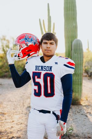 Football player in white Benson uniform number 50 poses with helmet by saguaro cactus.