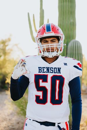 Football player in white Benson jersey gestures while standing near desert cactus.