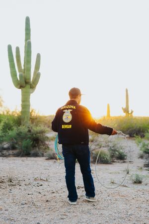 Person in Benson jacket practices roping at sunset among saguaro cacti.