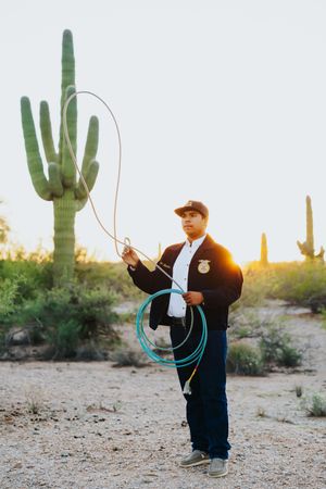 Person practicing rope tricks in desert landscape with saguaro cacti at sunset.