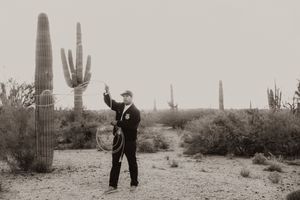 Black and white photo of person with lasso among saguaro cacti in desert.