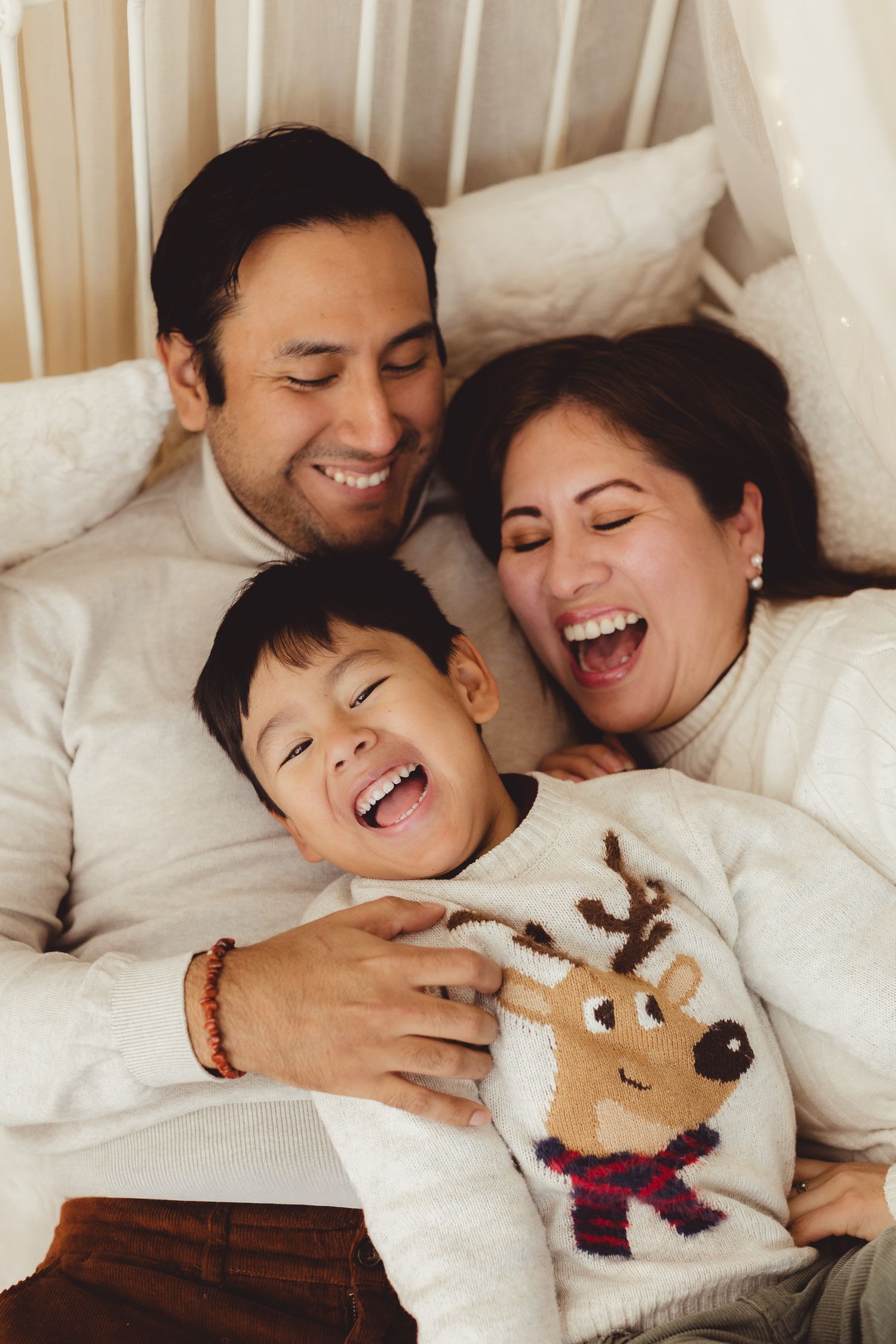 Family in white sweaters sharing joyful moment together on bed with stuffed toy.