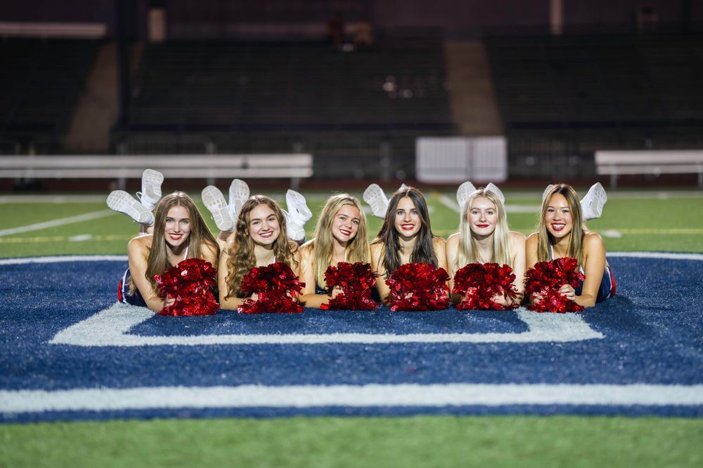 High school dancers in uniforms sitting in a line on blue and white striped football field.