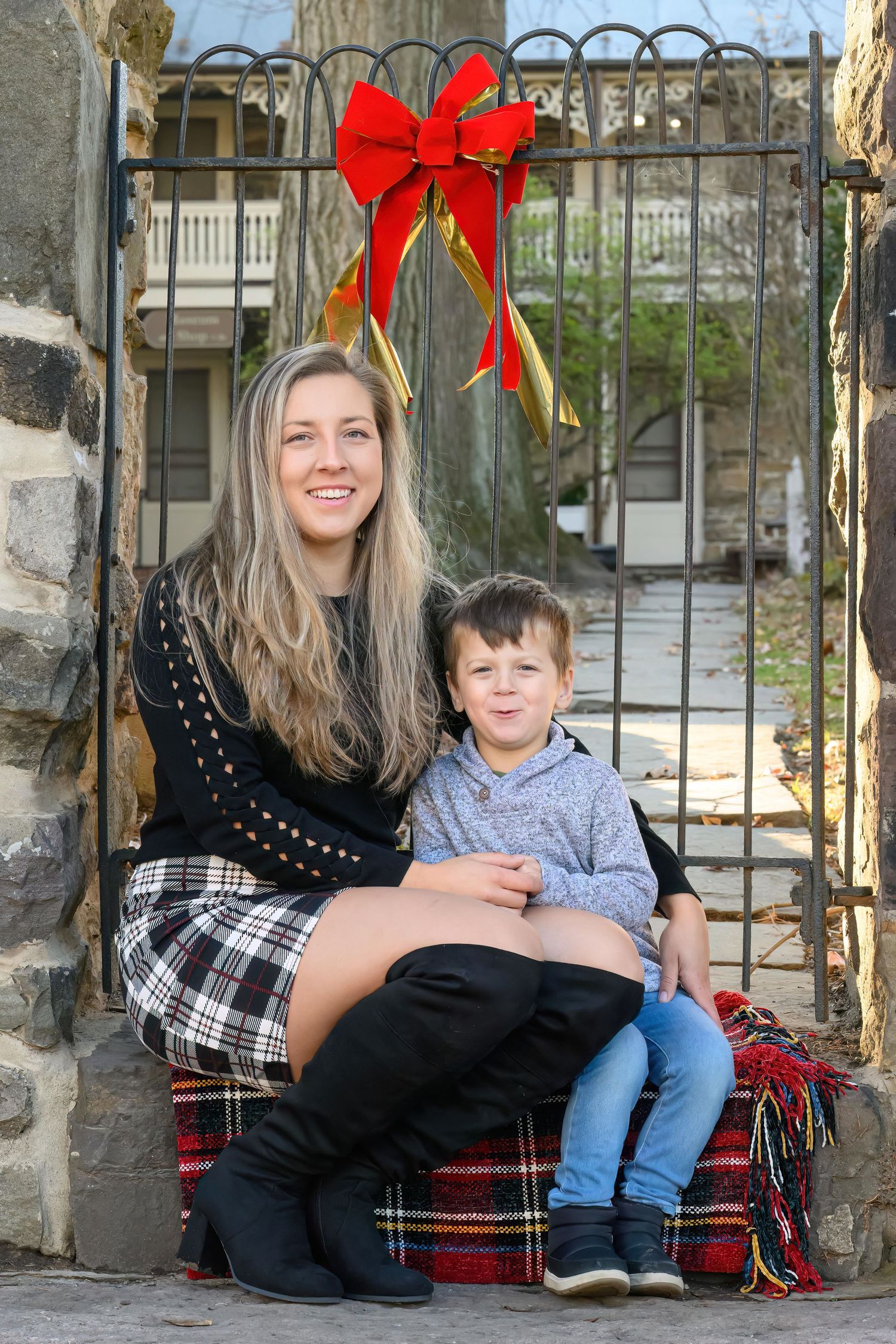 Christmas portrait on stone steps with plaid blanket and festive red bow decoration hanging above.