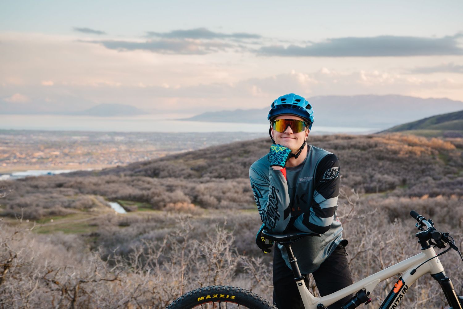 Mountain biker in blue jacket and helmet taking a break with scenic overlook view.