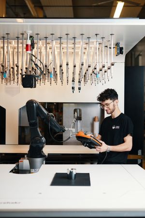 A barista prepares drinks at a modern coffee bar with hanging pendant lights and sleek white countertops.
