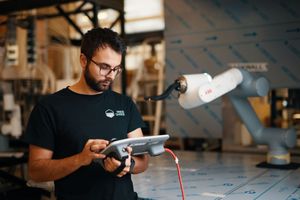 A person in a black t-shirt examines a white drone component in a workshop setting.