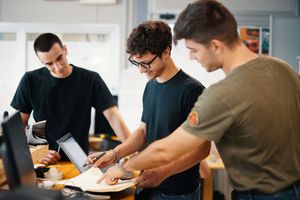 A group of people in black shirts sit at a table working together and taking notes during a meeting.