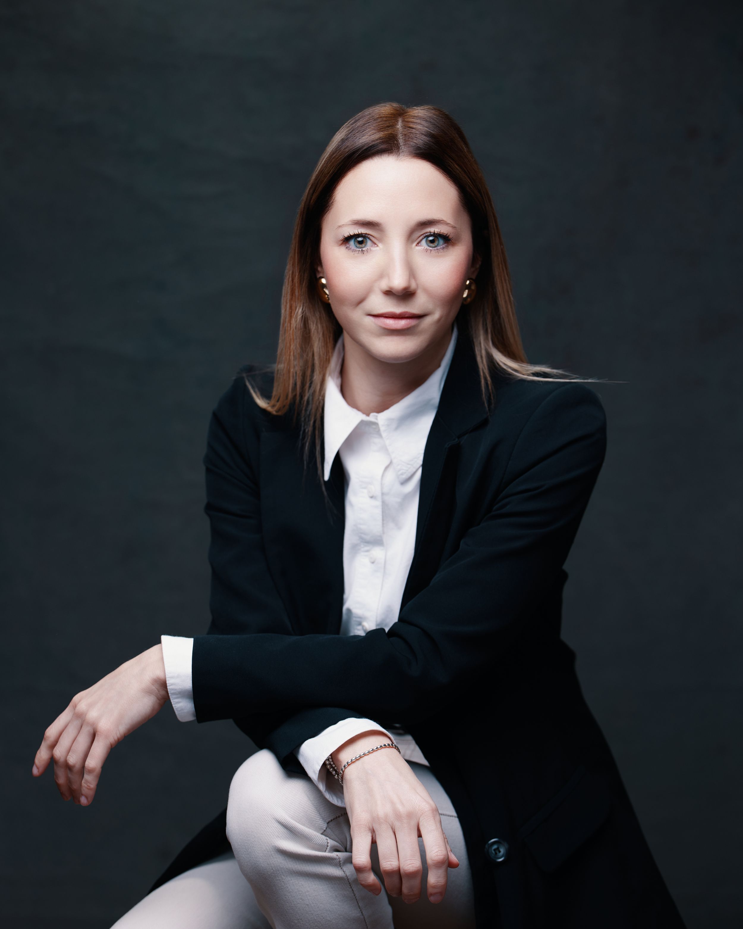 A professional business portrait against a dark background showcasing formal attire with a black blazer and white shirt.