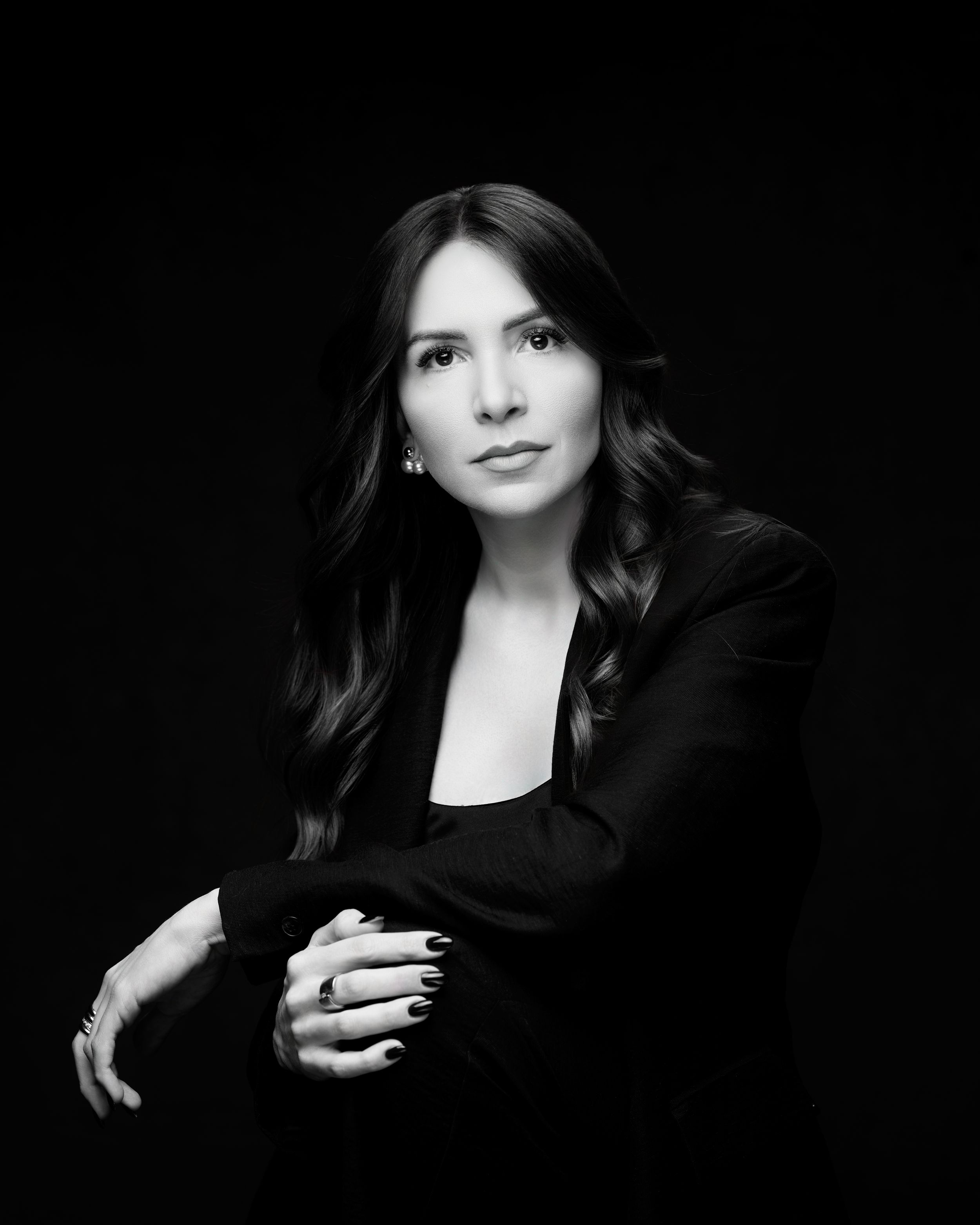 Professional black and white portrait of figure in dark blazer posed against black background in elegant style.
