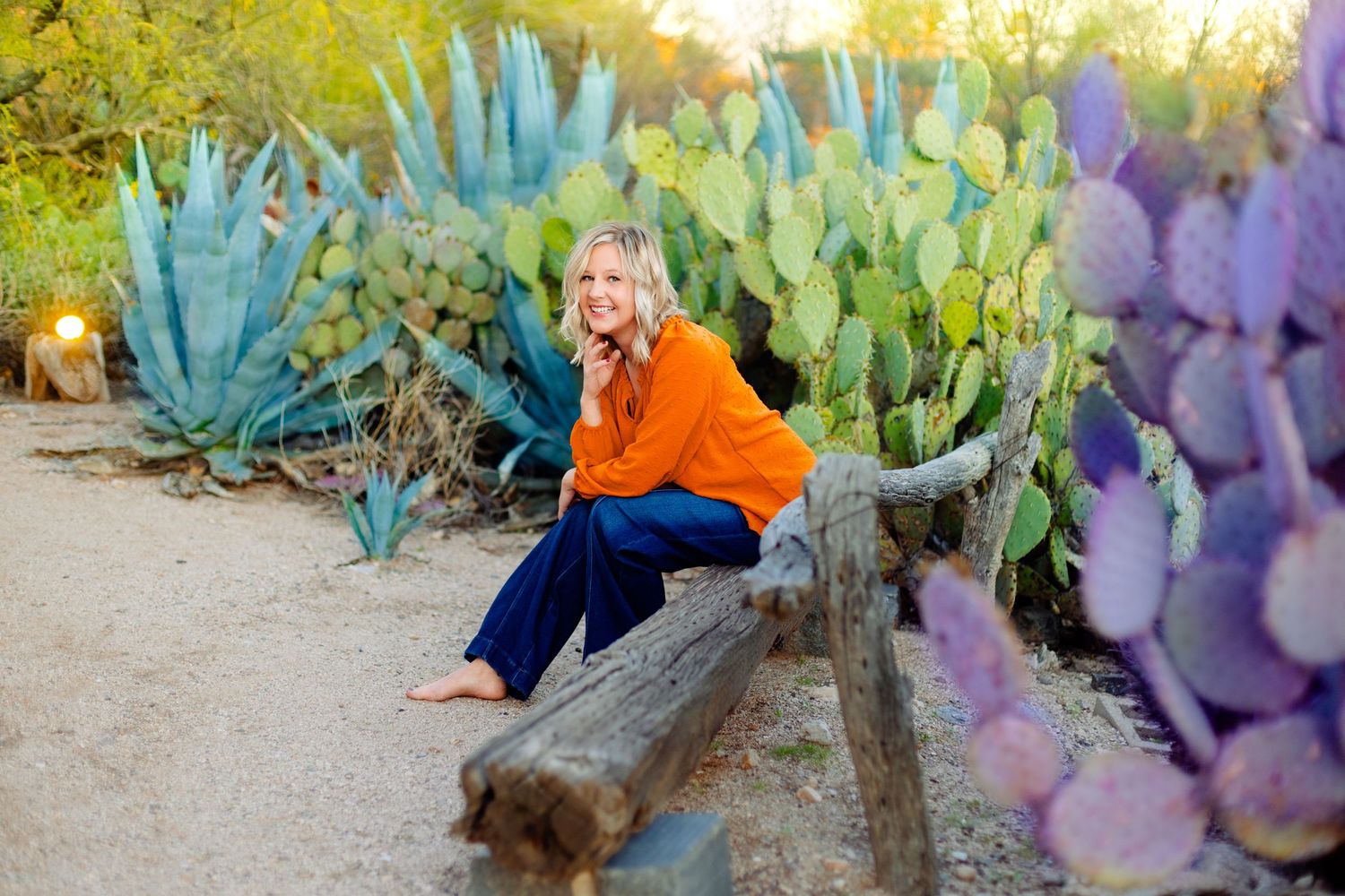 Lifestyle portrait on wooden log surrounded by colorful desert succulents and cacti.