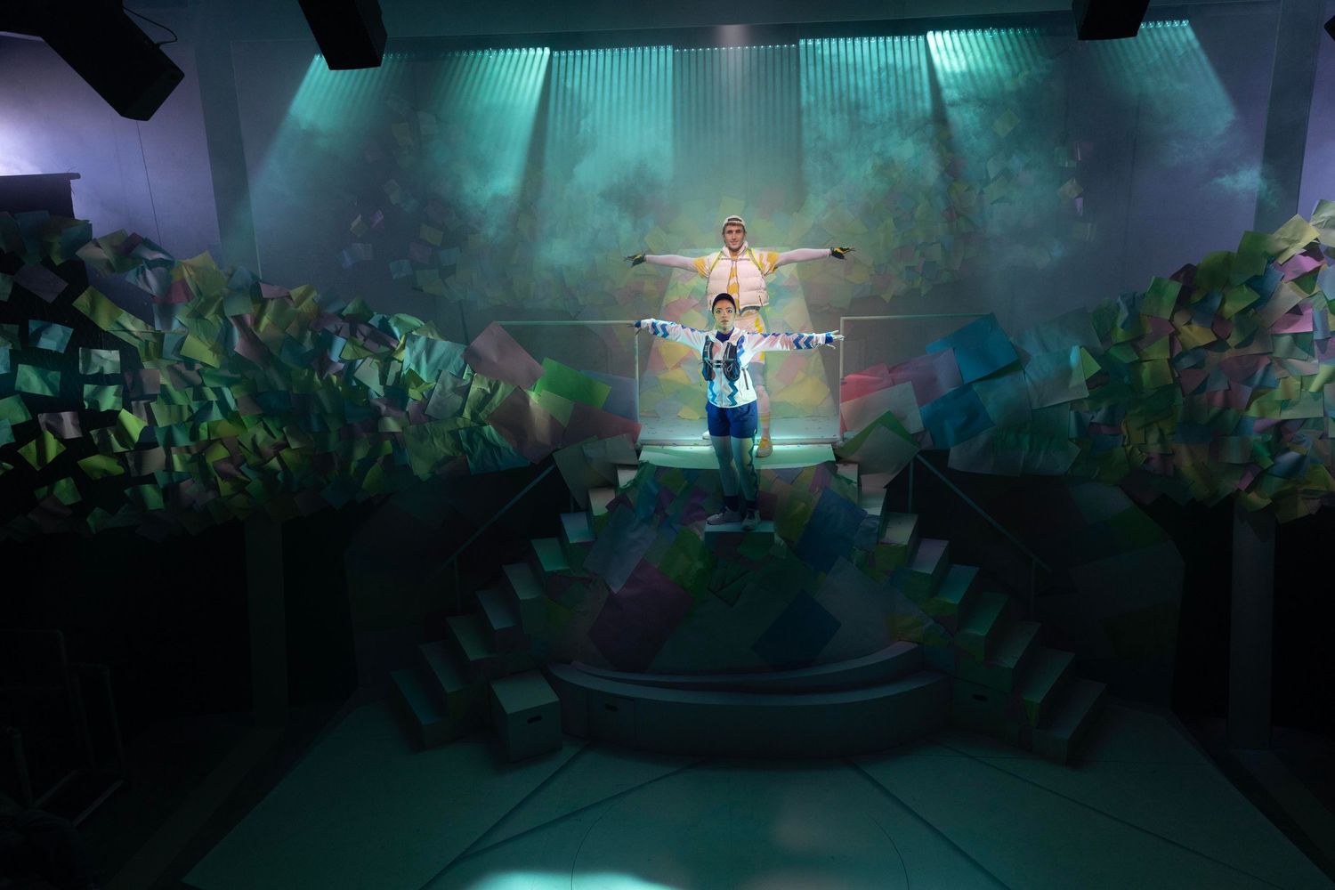 Theatrical scene with performer in ethereal green lighting surrounded by foliage set pieces.