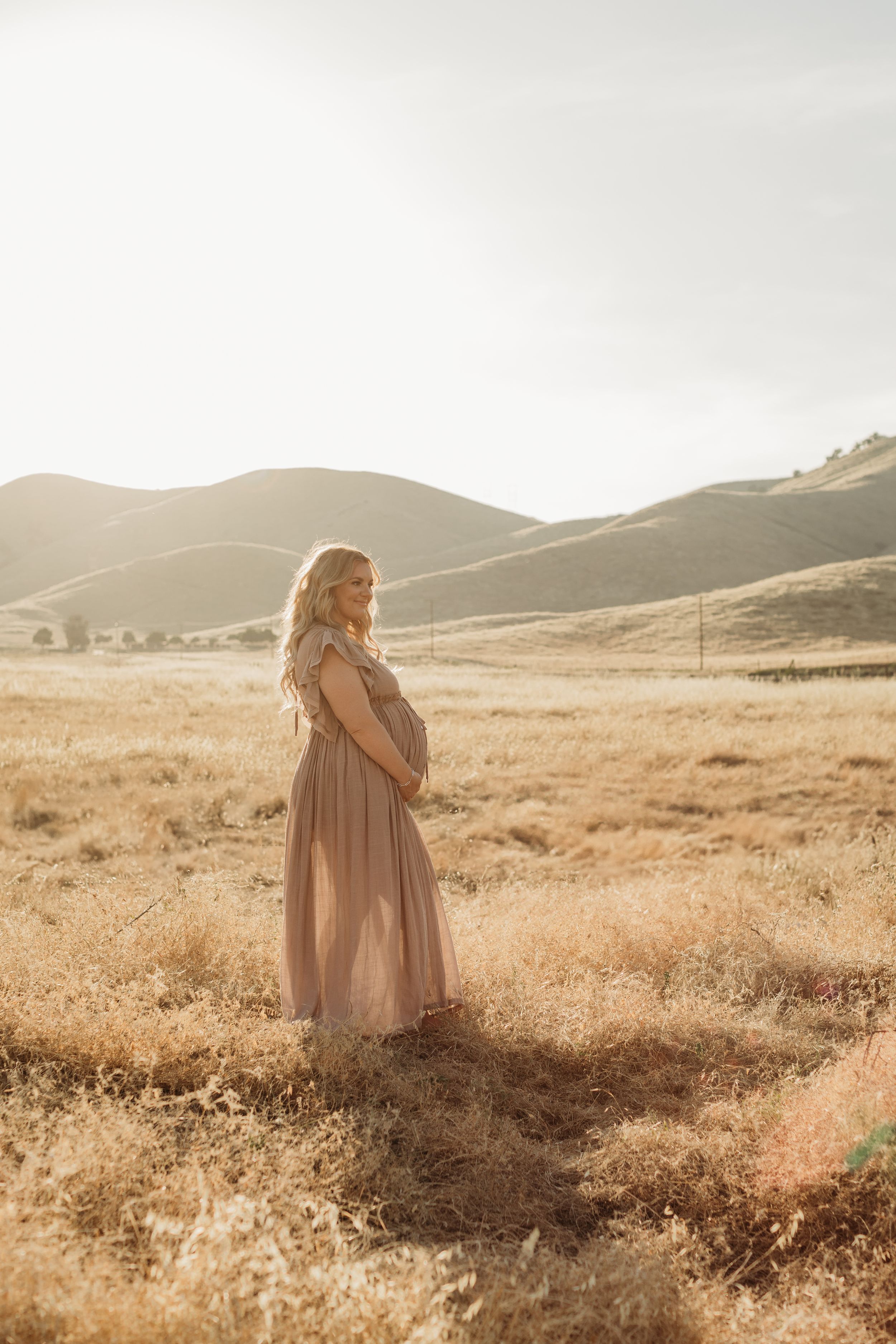 A serene maternity portrait in golden light with rolling hills in the background.