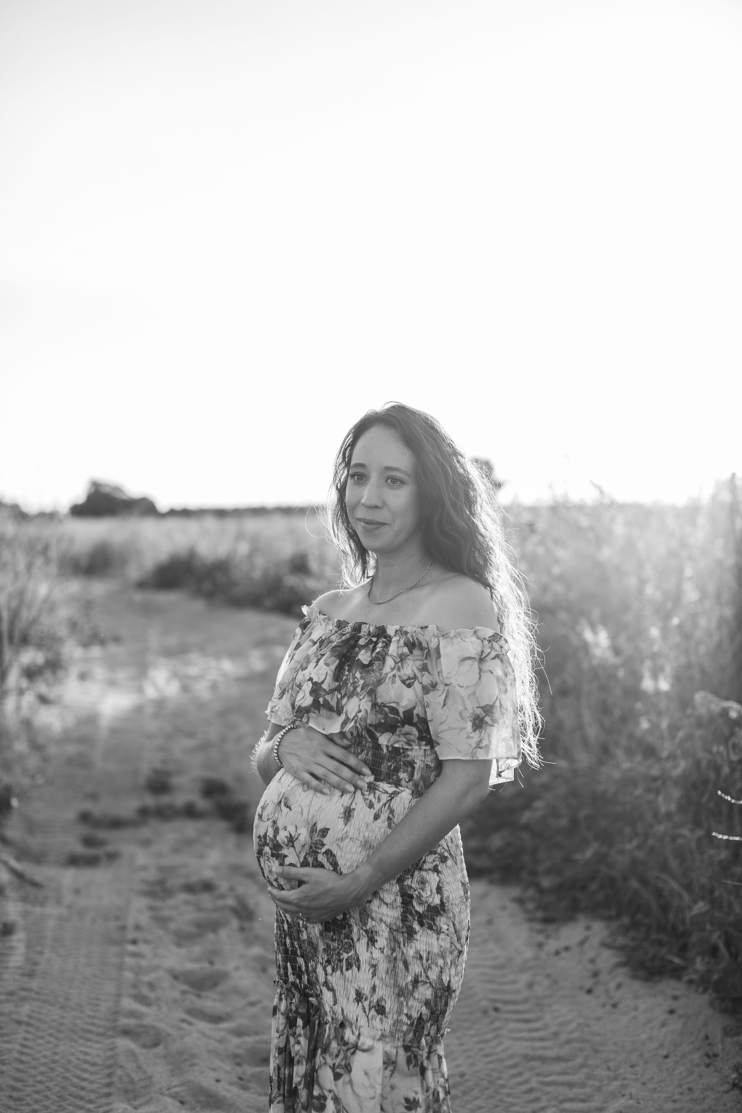 A black and white maternity photo capturing an expectant mother on a rural path.