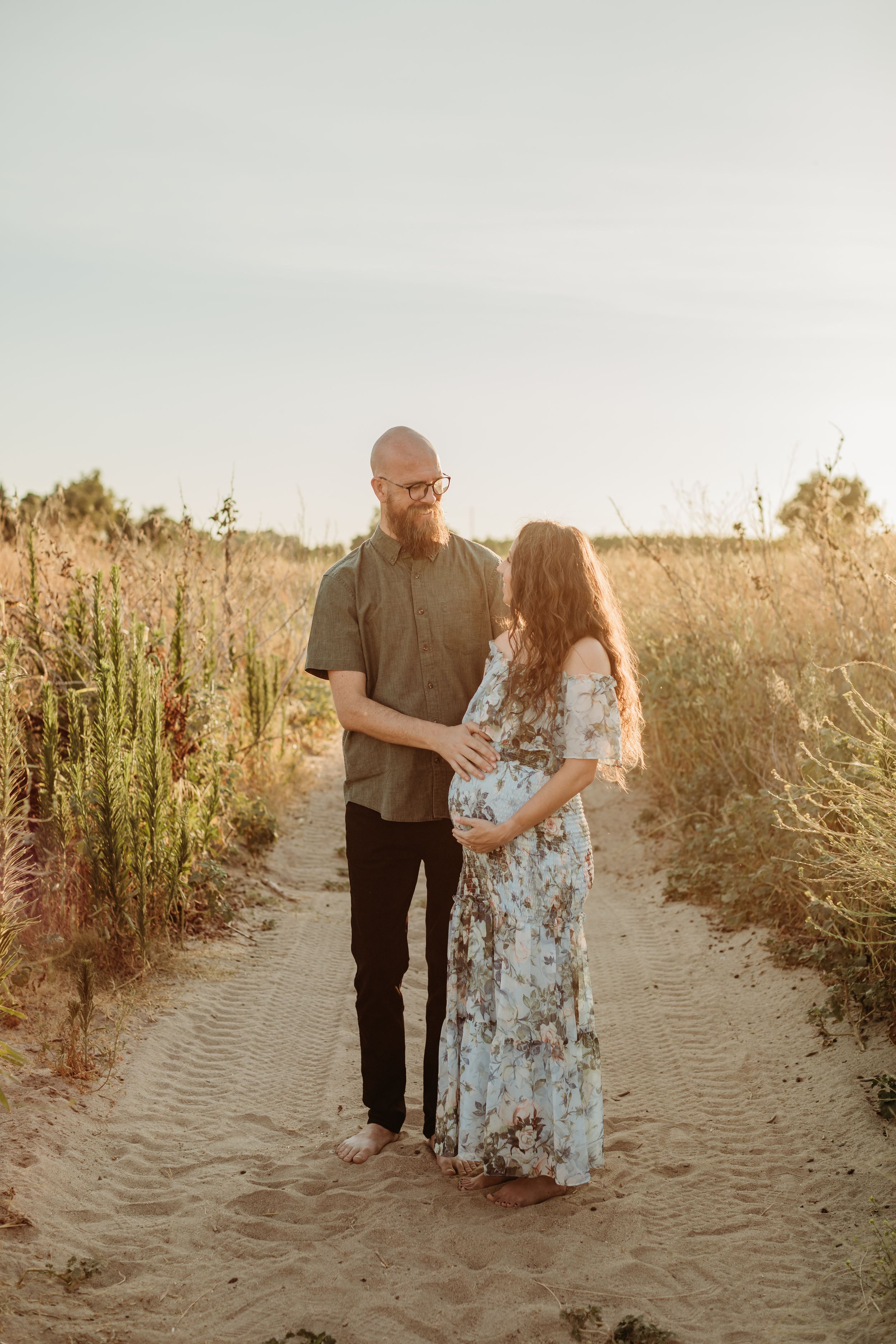 A couple shares an intimate moment during their maternity photoshoot on a nature path.