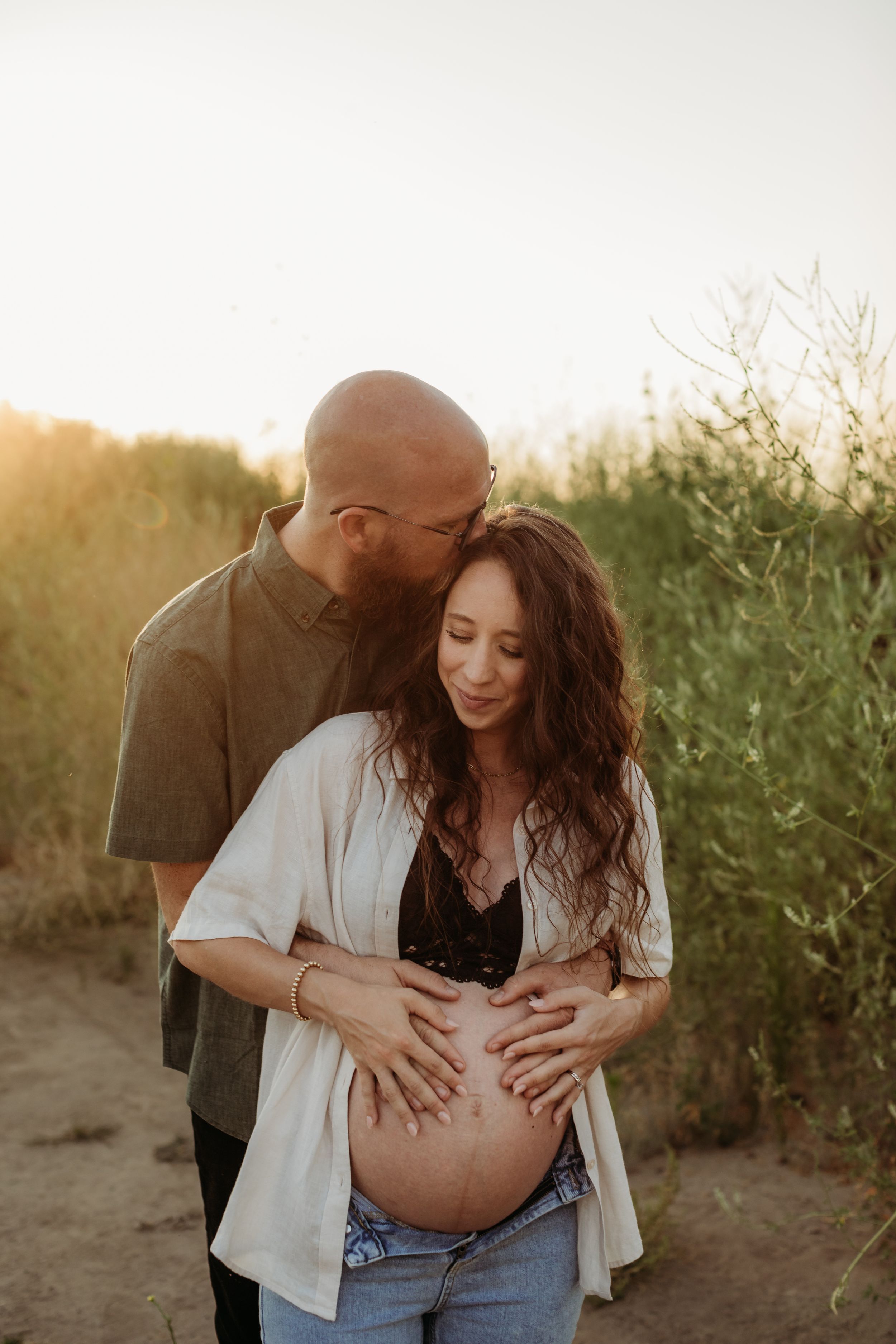 A tender moment between expectant parents during golden hour outdoors.
