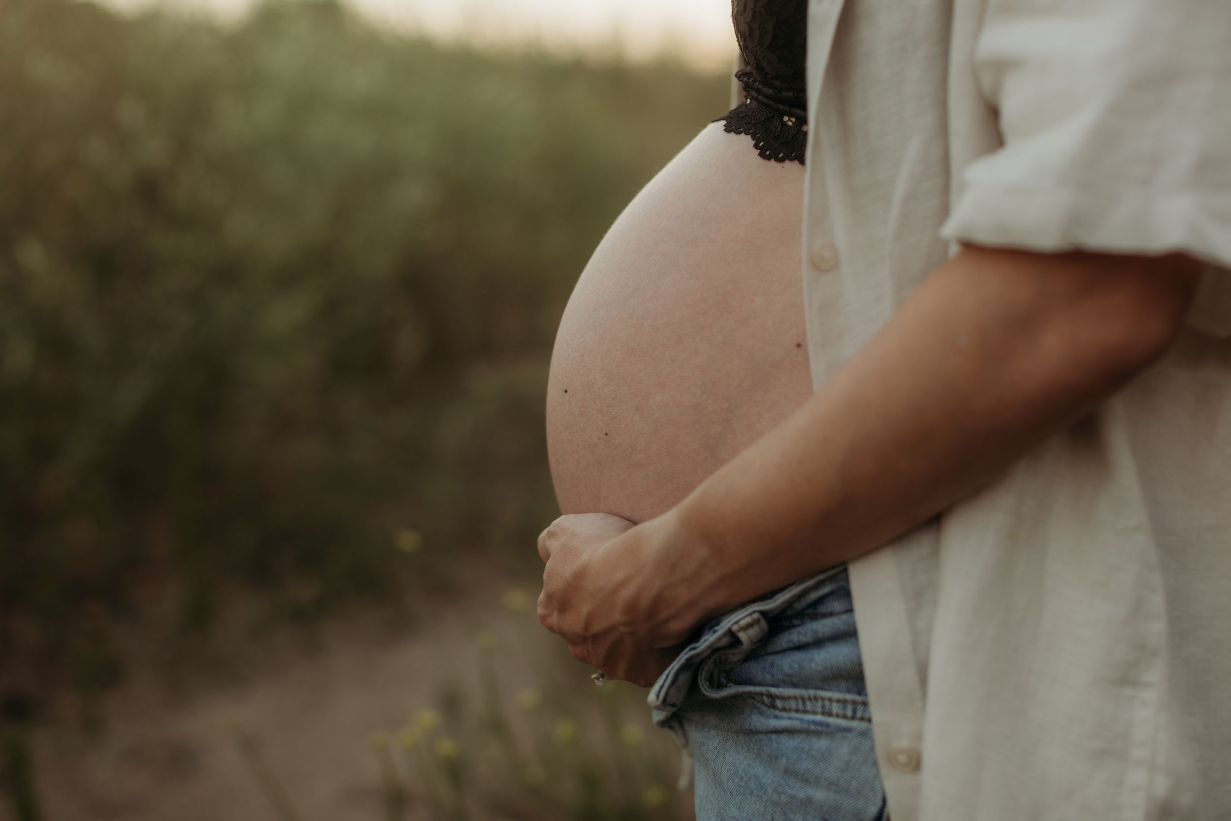 Close-up shot of expecting parents hands cradling a pregnant belly.